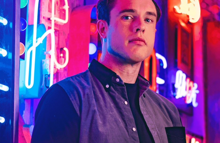 Headshot of Ed Gamble with neon lights behind him