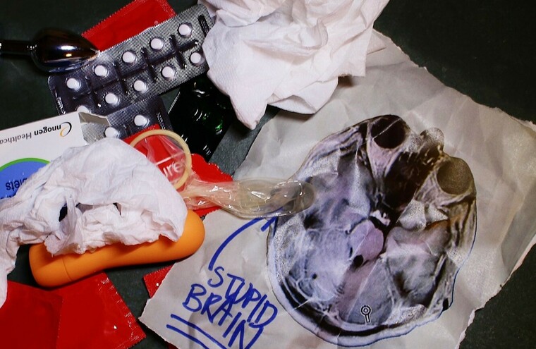 A photograph of a random selection of items including pills, condom, tissues and a note that reads 'Stupid Brain'