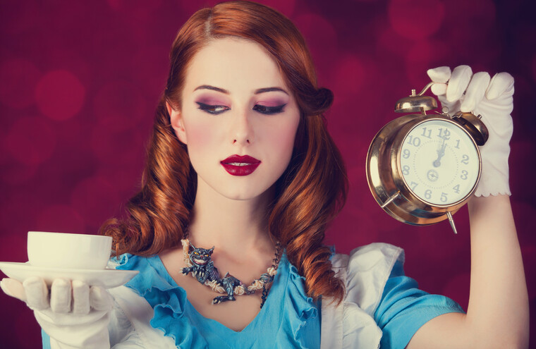 A woman dressed as Alice. She holds a cup and saucer in one hand, and an alarm clock in the other.