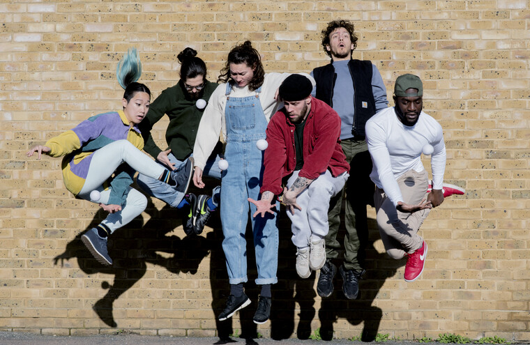 A group of dancers jump against a brick wall.