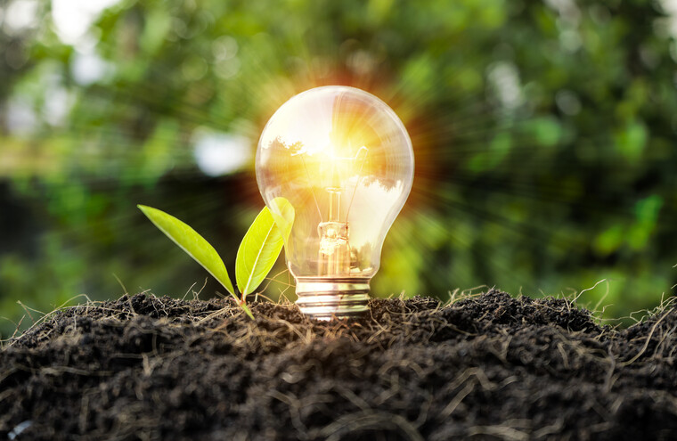A lightbulb glowing with light. It has been planted in a mound of soil.