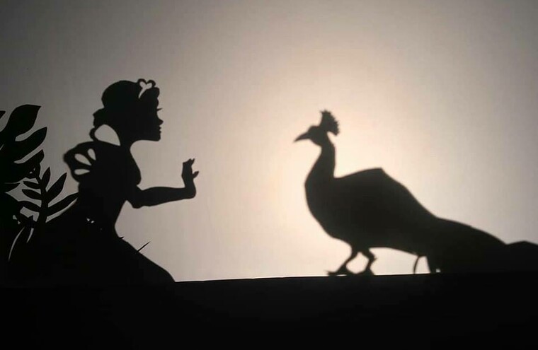 Shadow puppets of a girl and a peacock facing one another.