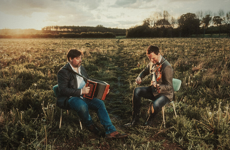 Spiers & Boden are sat in a field playing musical instruments