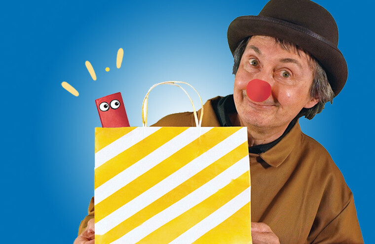 A man with a red nose holds a white and yellow striped paper bag. A smaller red paper bag with googly eyes pokes out the top.