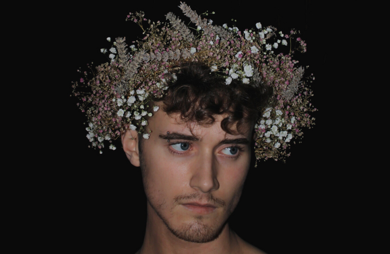 A man on a black background wears a crown made out of flowers.