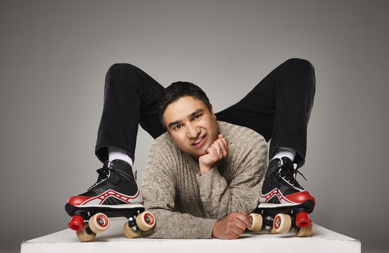 Nick Mohammed with legs over his shoulders wearing roller skates.