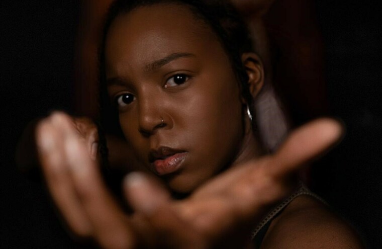 A woman stands with her hand out, blurred silhouettes stand behind her.