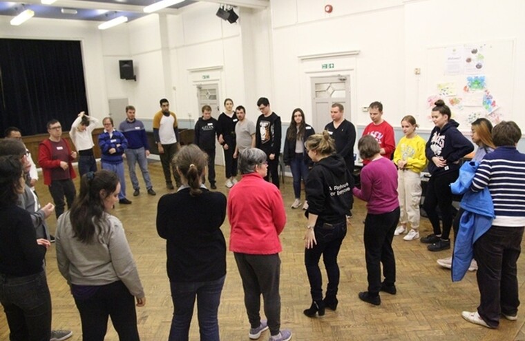 A group of young adults participating in a workshop. They are all stood in a circle in the middle of a room.