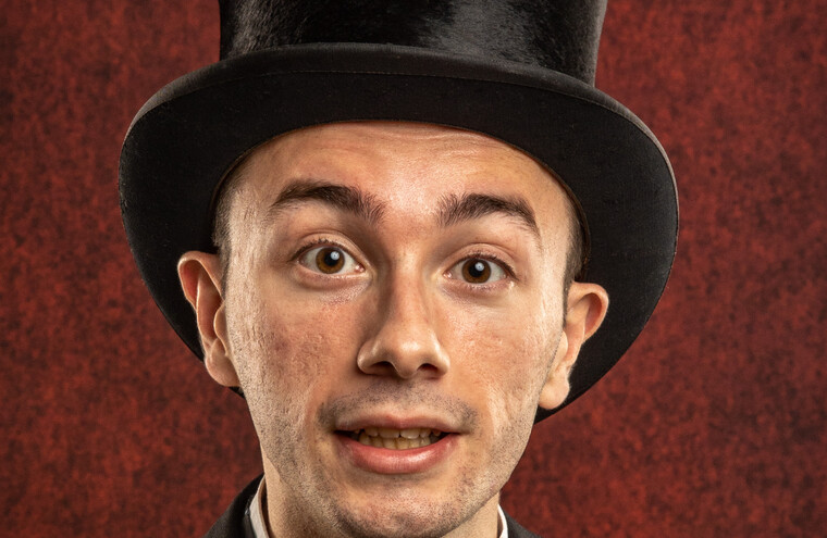 Closeup of a man dressed in a black top hat, white shirt, black tie and black suit jacket.