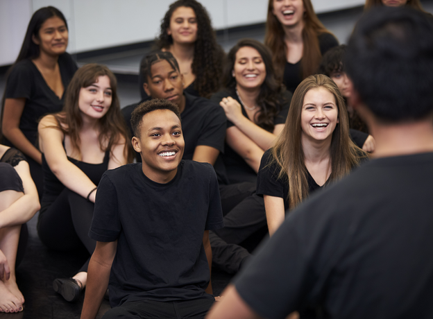 A group of young adults listening to someone speak. Some of them are smiling.