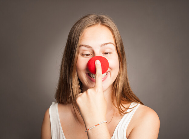 A woman smiling as she puts on a red clown nose.